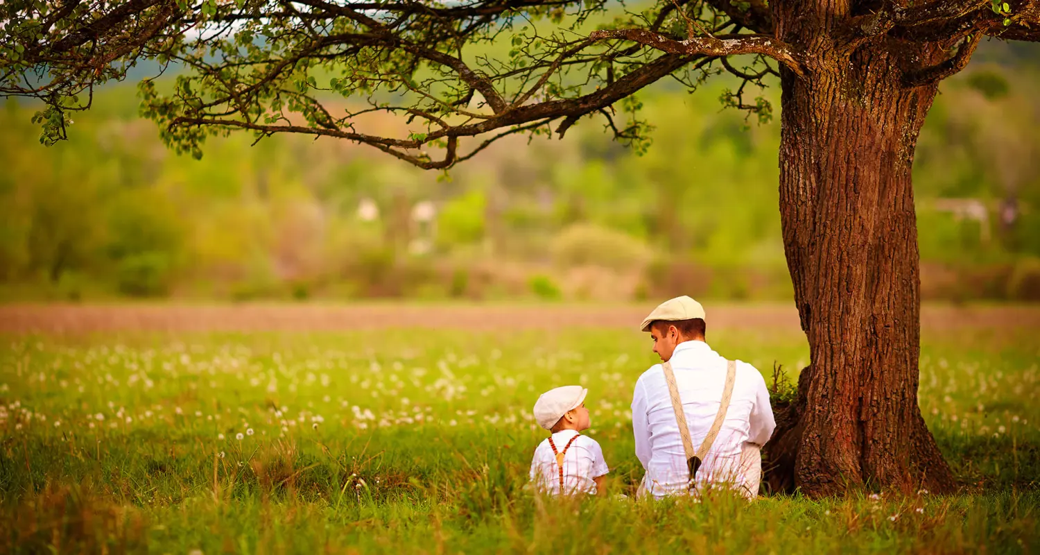 Vater und Sohn sitzen unter dem Baum auf dem Frühlingsrasen